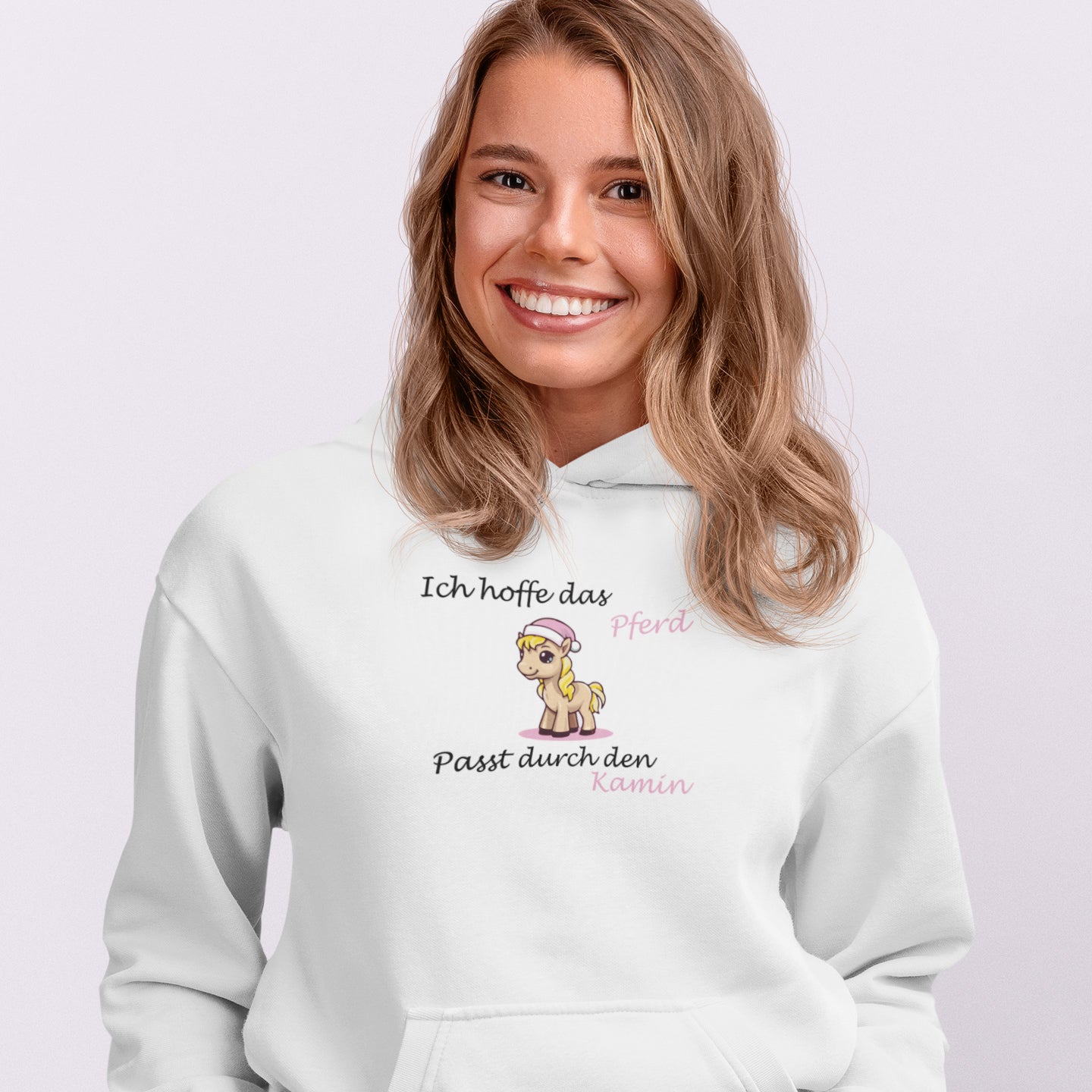 Eine blonde Frau trägt einen weißen Weihnachtspullover auf dem ein Pferd und der Spruch "Ich hoffe das Pferd passt durch den Kamin" steht